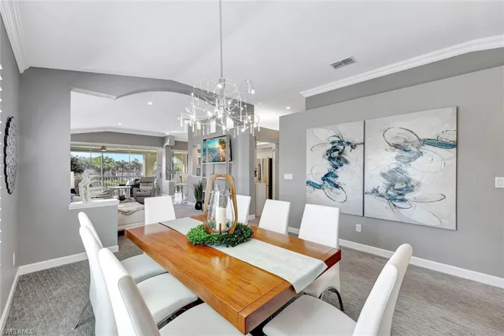 Carpeted dining room with a notable chandelier, lofted ceiling, and crown molding