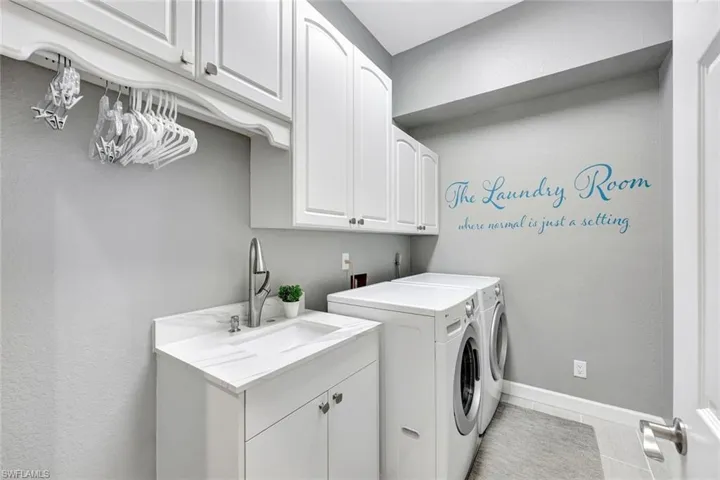 Laundry area with washer and clothes dryer, cabinets, light tile patterned floors, and sink
