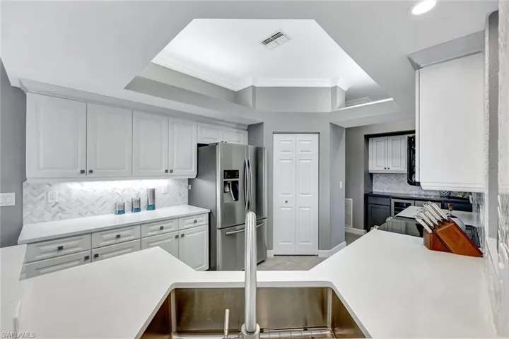 Kitchen with decorative backsplash, a kitchen breakfast bar, crown molding, stainless steel fridge with ice dispenser, and white cabinetry