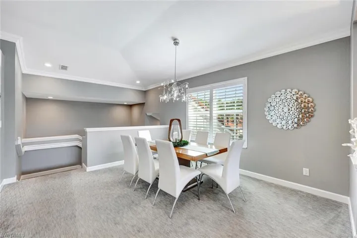Carpeted dining room with a notable chandelier and ornamental molding