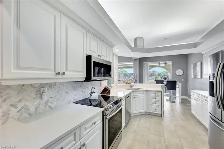 Kitchen with tile backsplash, white cabinets, waterfall quartz countertops, sink, light tile patterned floors, and appliances with stainless steel finishes.
