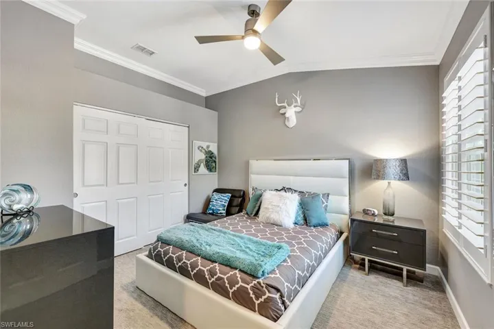 Bedroom with ceiling fan, ornamental molding, and light carpet