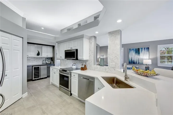 Kitchen with sink, decorative backsplash, appliances with stainless steel finishes, white cabinetry, and beverage cooler