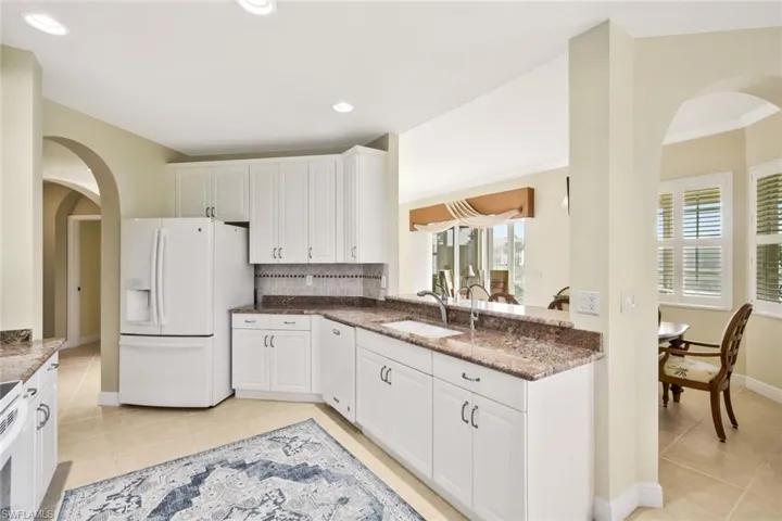 Kitchen with arched walkways, white appliances, dark stone countertops, white cabinetry, and light tile patterned floors