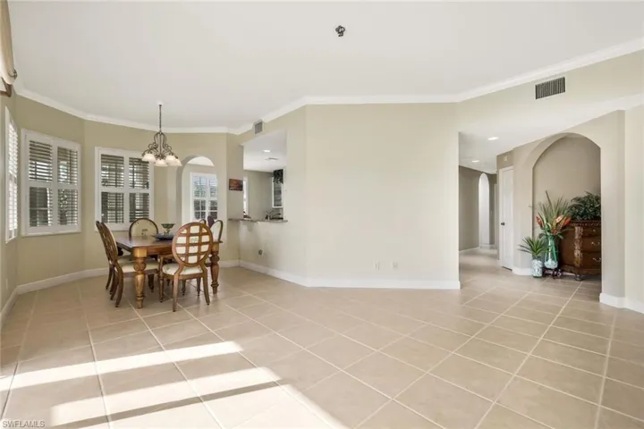 Dining room featuring arched walkways, light tile patterned floors, crown molding, and suspended lighting