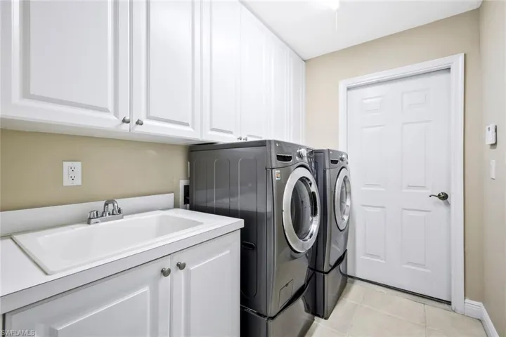 Laundry room with separate washer and dryer, light tile patterned floors, and cabinet space