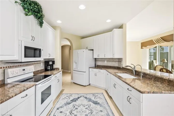 Kitchen featuring white appliances, dark stone countertops, arched walkways, white cabinetry, and recessed lighting