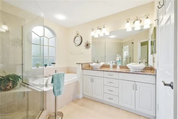 Bathroom featuring double vanity, a shower stall, a garden tub, and light tile patterned flooring