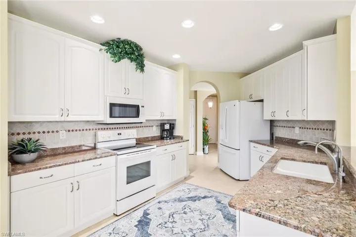 Kitchen with arched walkways, white appliances, white cabinets, and recessed lighting
