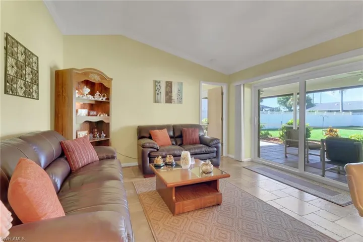 Living room featuring vaulted ceiling, ornamental molding, and stone tile flooring