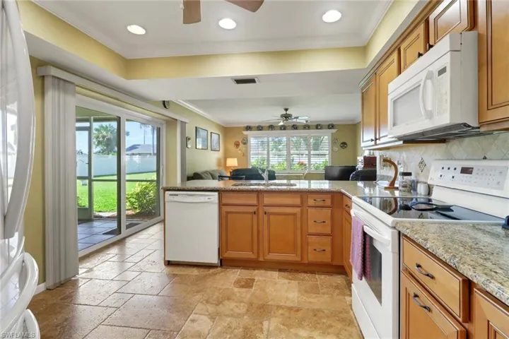 Kitchen with white appliances, ornamental molding, open floor plan, brown cabinets, and a peninsula