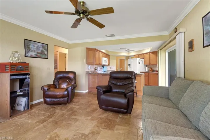 Living room featuring ceiling fan, crown molding, and light stone finish flooring