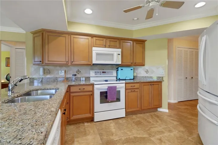 Kitchen with ornamental molding, white appliances, brown cabinetry, light stone counters, and decorative backsplash