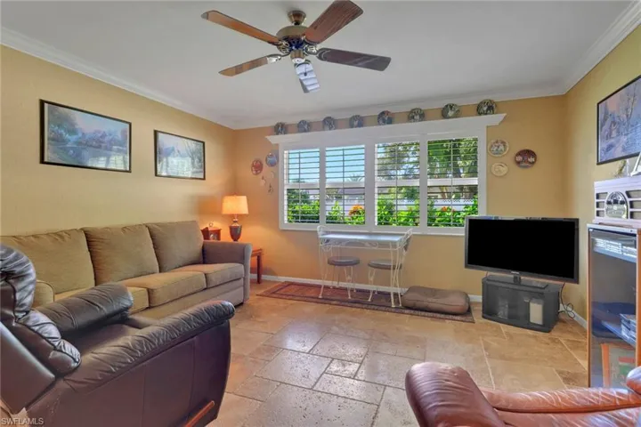 Living area featuring ornamental molding, stone tile flooring, and a ceiling fan