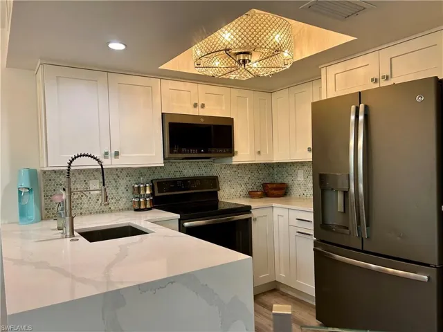 Modern kitchen featuring white shaker cabinetry, patterned tile backsplash, and quartz countertops with integrated sink