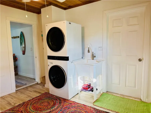 Dedicated laundry area featuring a stacked washer and dryer, utility sink with a tongue and grove wood ceiling.