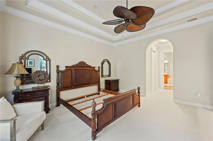Carpeted bedroom featuring crown molding, connected bathroom, a tray ceiling, and ceiling fan