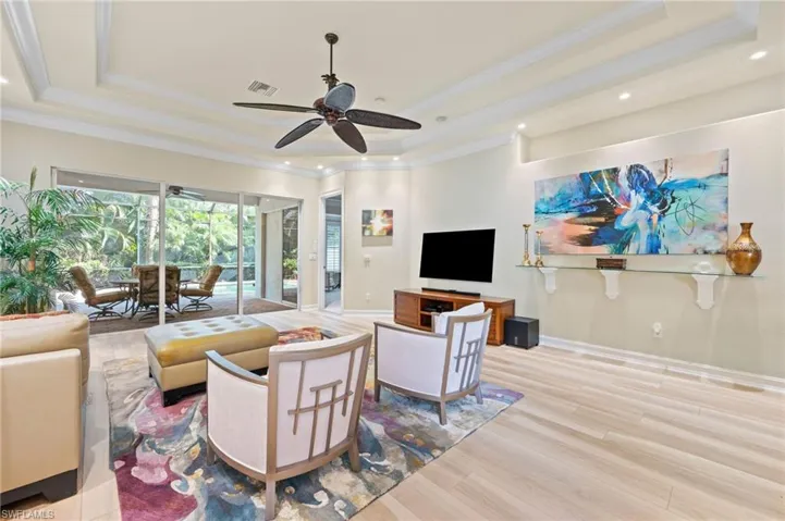 Living room featuring ceiling fan, a raised ceiling, crown molding, and luxury style floors