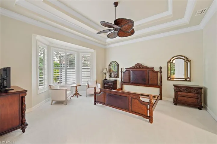 Carpeted bedroom with ceiling fan, a raised ceiling, and crown molding