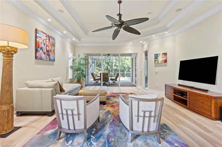 Living room featuring ceiling fan, a raised ceiling, crown molding, and luxury style floors