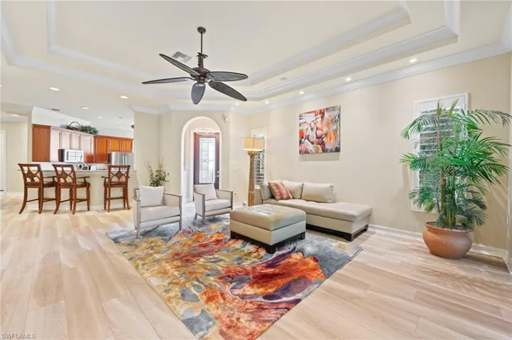 Living room featuring ceiling fan, a raised ceiling, crown molding, and luxury style floors