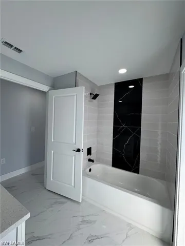 Bathroom featuring washtub / shower combination, marble look tile flooring, recessed lighting, vanity, and baseboards
