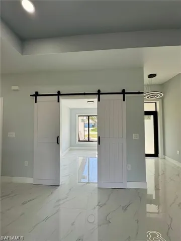 Unfurnished room featuring a barn door, baseboards, and light marble finish floors