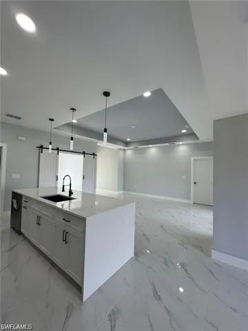 Kitchen with a sink, a barn door, baseboards, light marble finish floors, and recessed lighting