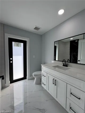 Bathroom featuring vanity, toilet, marble finish floors, baseboards, and recessed lighting