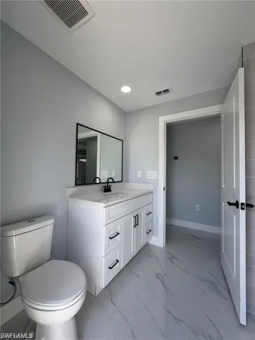 Bathroom featuring vanity, toilet, marble look tiles, recessed lighting, and baseboards
