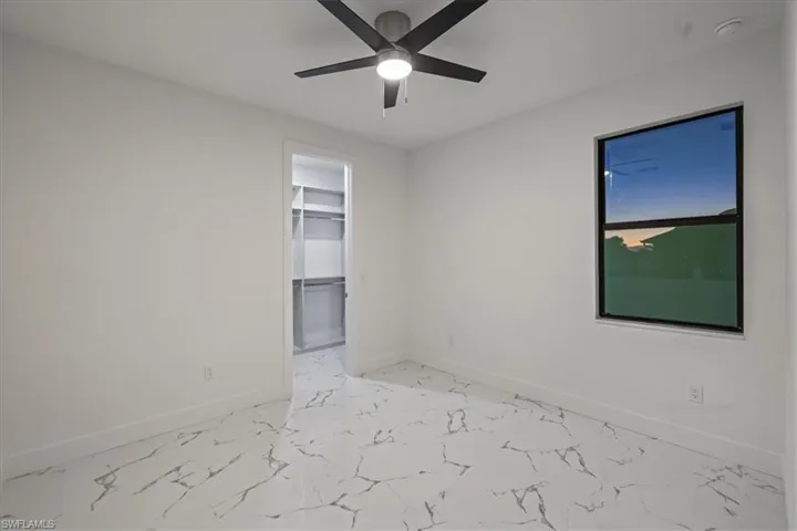 Empty room with marble finish floor, baseboards, and ceiling fan