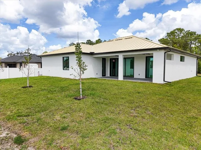 Rear view of house featuring stucco siding, fence, and a lawn