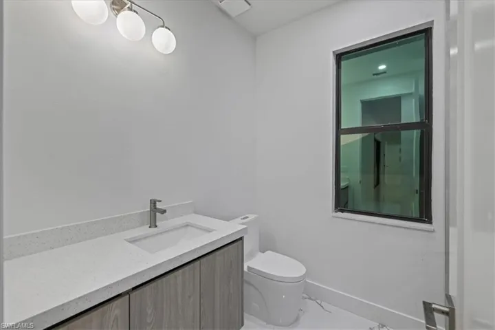 Half bath with marble finish floor, baseboards, toilet, and vanity