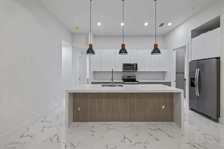 Kitchen featuring tasteful backsplash, stainless steel appliances, marble finish floor, a sink, and white cabinets