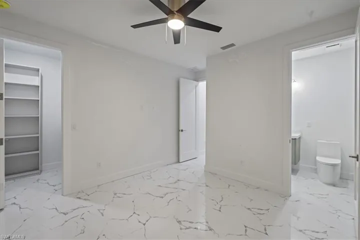 Unfurnished bedroom featuring connected bathroom, a walk in closet, marble finish floor, baseboards, and visible vents