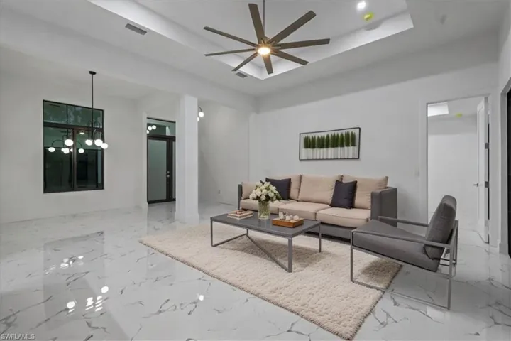 Living area featuring a tray ceiling, ceiling fan with notable chandelier, marble finish floor, and visible vents