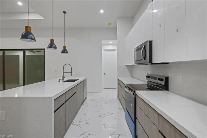Kitchen with marble finish floor, a sink, modern cabinets, and appliances with stainless steel finishes