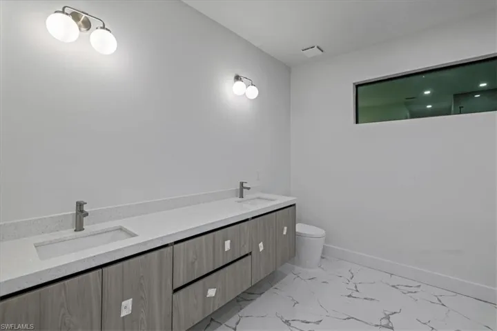 Full bath with marble finish floor, toilet, a sink, and baseboards