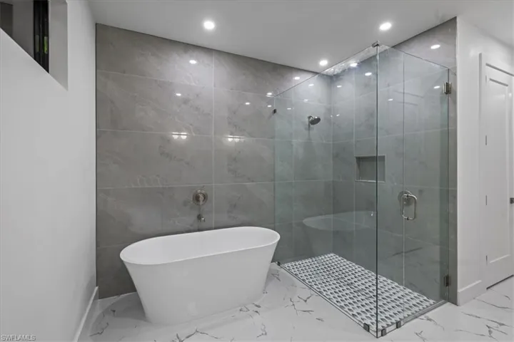 Full bath featuring marble finish floor, a freestanding tub, recessed lighting, and a shower stall