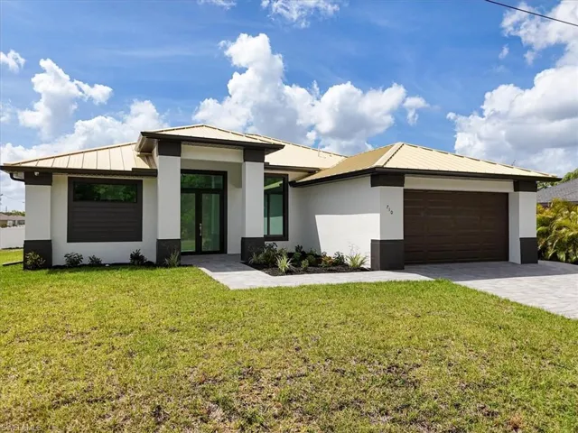View of front of home with stucco siding, an attached garage, metal roof, decorative driveway, and a front yard