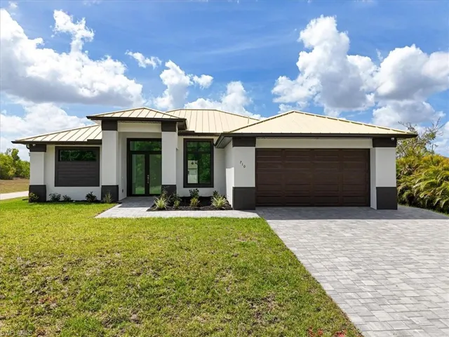 View of front facade with a standing seam roof, french doors, stucco siding, metal roof, and a garage