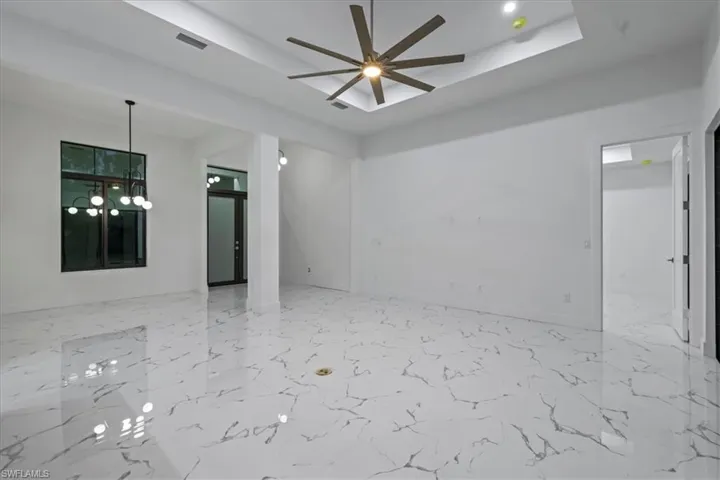 Unfurnished room with a tray ceiling, baseboards, marble finish floor, and ceiling fan