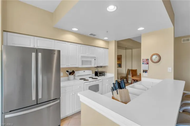 Kitchen with white appliances, light countertops, recessed lighting, white cabinets, and light tile patterned flooring