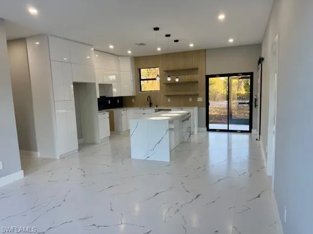 Kitchen featuring open shelves, modern cabinets, hanging light fixtures, white cabinets, and a kitchen island