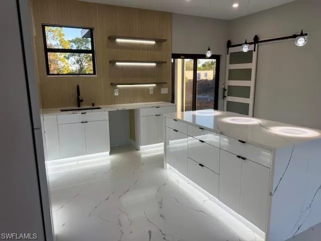 Kitchen featuring modern cabinets, white cabinets, open shelves, light stone countertops, and a barn door