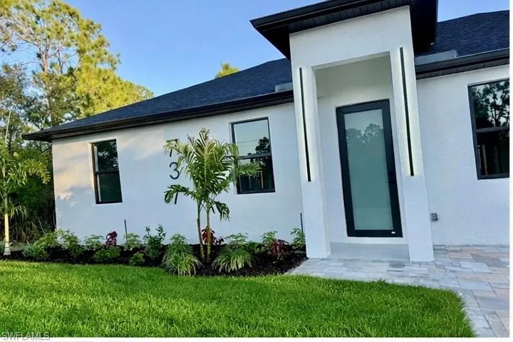 Entrance to property with a yard, a shingled roof, and stucco siding
