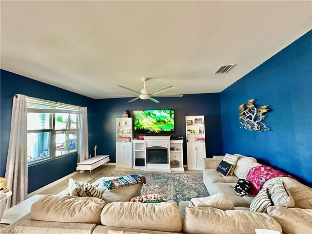 Living room featuring visible vents, a glass covered fireplace, and a ceiling fan