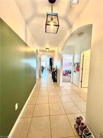 Corridor with light tile patterned floors, arched walkways, baseboards, and vaulted ceiling