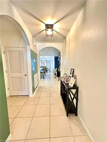 Corridor with light tile patterned flooring, arched walkways, and baseboards