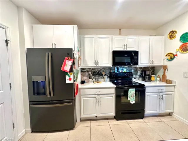 Kitchen featuring white cabinets, light countertops, light tile patterned flooring, and black appliances